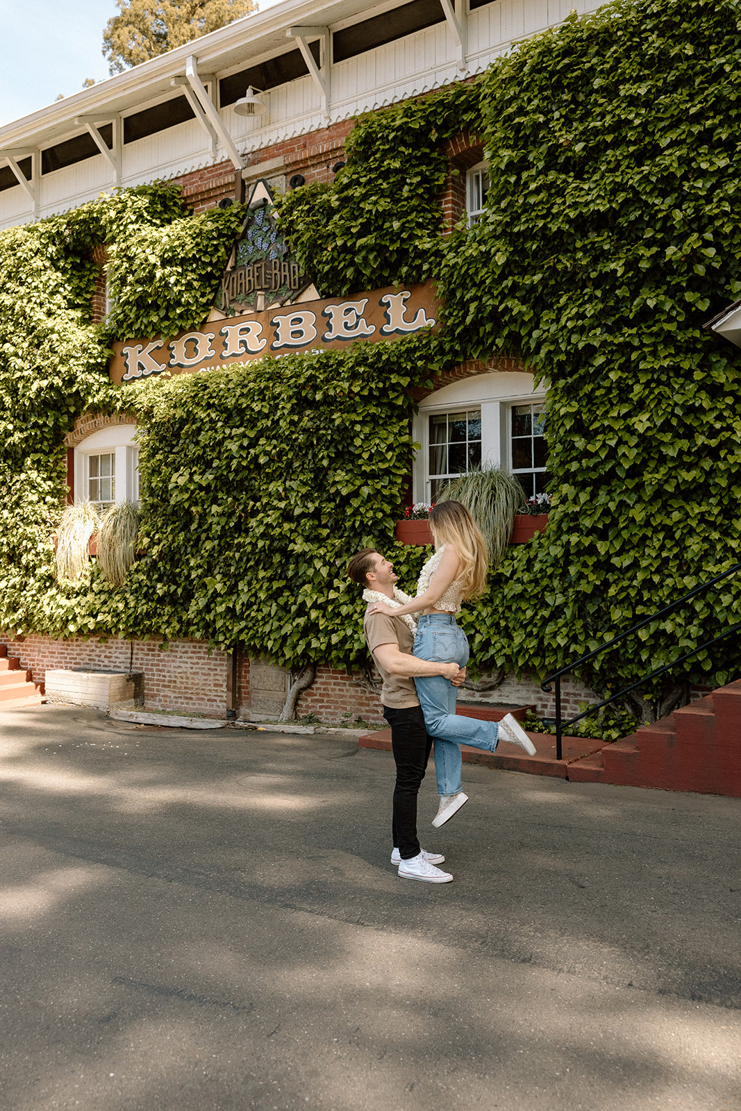 Abel lifting Aidan outside the ivy-covered Korbel winery during their engagement celebration